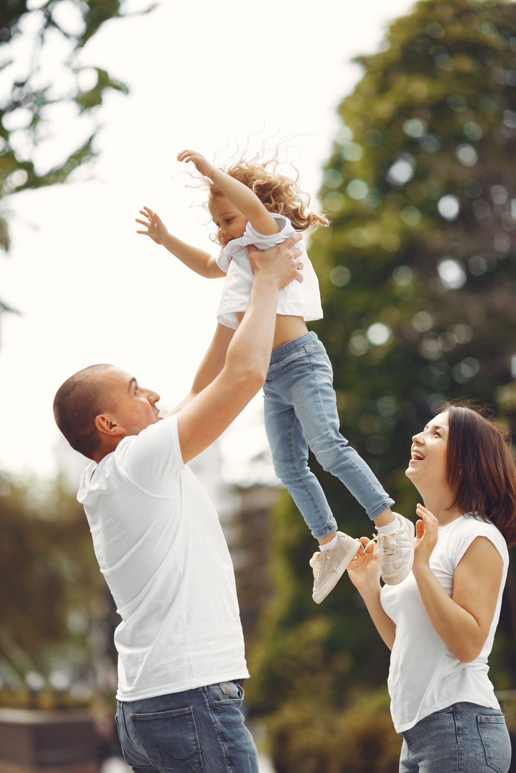 Joyful parents playing with their daughter in the park during a sunny day, embodying family love.